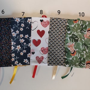 Puede incluir: Cinco fundas de libro de tela diferentes con lazos de cinta. Las fundas presentan varios patrones, incluyendo flores, corazones, geom&eacute;tricos y hojas tropicales con un retrato de Frida Kahlo.