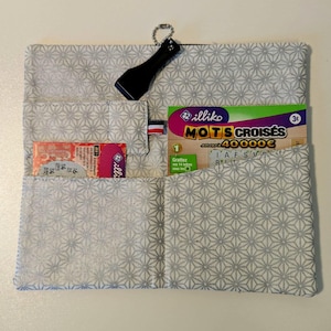 May include: A gray fabric wallet with a geometric pattern, featuring multiple pockets. It holds a black keychain flashlight, a lottery ticket, and a scratch-off ticket. The wallet is open, displaying its contents.