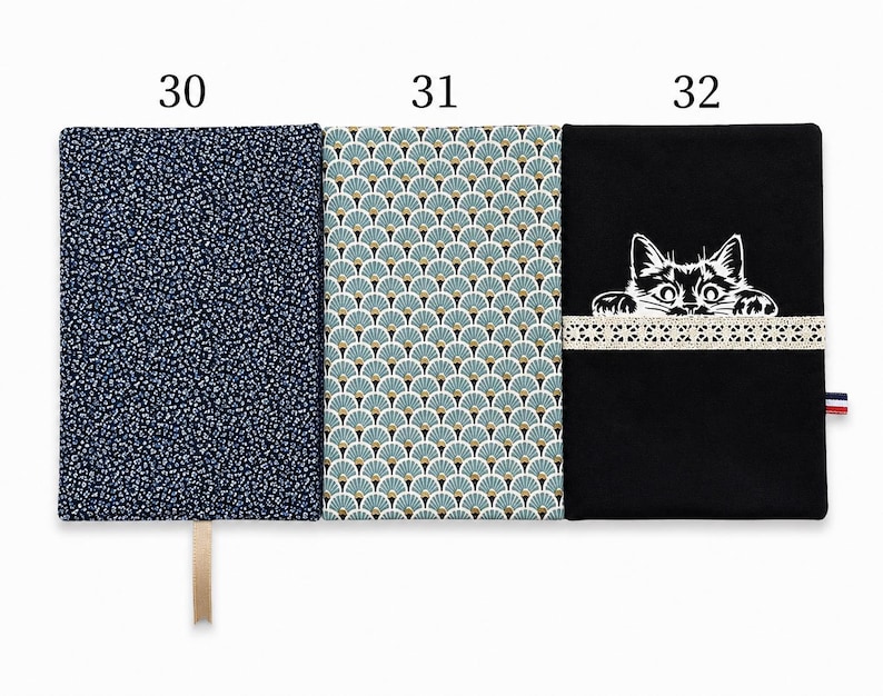 May include: Three rectangular fabric book covers labeled 30, 31, and 32. Cover 30 is dark blue with a small white floral pattern. Cover 31 features a teal and gold fan-shaped pattern. Cover 32 is black with a white cat graphic and lace trim.