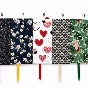May include: Five rectangular fabric book covers labeled 6 through 10. Patterns include small colorful shapes on black, white cherry blossoms on navy, red hearts on white, black and gold art deco fans, and green monstera leaves with Frida Kahlo.