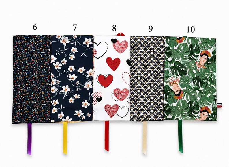 May include: Five rectangular fabric book covers labeled 6 through 10. Patterns include small colorful shapes on black, white cherry blossoms on navy, red hearts on white, black and gold art deco fans, and green monstera leaves with Frida Kahlo.