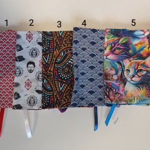 Puede incluir: Cinco cubiertas de libros diferentes con varios dise&ntilde;os. Las cubiertas est&aacute;n hechas de tela y tienen cintas de diferentes colores atadas a ellas. Los dise&ntilde;os incluyen un patr&oacute;n geom&eacute;trico rojo y blanco, un patr&oacute;n blanco y negro con la cara de un hombre, un patr&oacute;n paisley negro y naranja, un patr&oacute;n de olas azul y blanco y un patr&oacute;n de gato colorido.