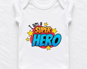 May include: A white short-sleeved baby bodysuit featuring a graphic design with the text I am a SUPER HERO in blue and orange letters. The text is set against a red comic-book style speech bubble shape surrounded by small yellow stars.