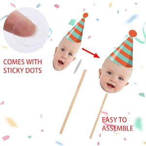 May include: Party decorations featuring baby faces with party hats. The image shows two baby face cutouts with party hats, wooden sticks, and sticky dots for assembly. Text on the image reads "COMES WITH STICKY DOTS" and "EASY TO ASSEMBLE".