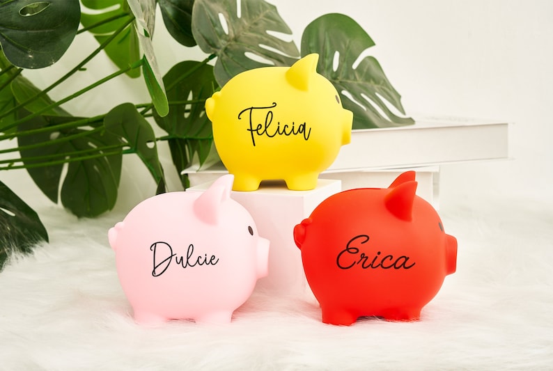 May include: Three piggy banks, one yellow, one pink, and one red, with names written on them: Felicia, Dulcie, and Erica.