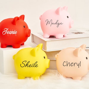 May include: Four piggy banks with personalized names: Jeanie, Madge, Sheile, and Cheryl. The piggy banks are red, pink, yellow, and light pink.