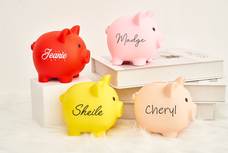 May include: Four piggy banks with personalized names: Jeanie, Madge, Sheile, and Cheryl. The piggy banks are red, pink, yellow, and light pink.