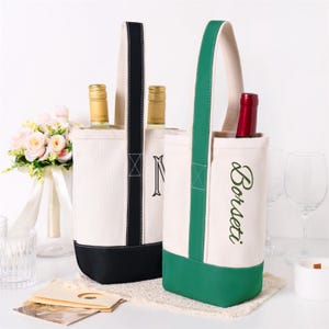 May include: Two canvas wine bottle bags with tall handles. One bag features a black base and handle with a partial letter N visible. The other bag has a green base and handle with the embroidered text Borseti in green, containing a red wine bottle.