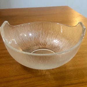 May include: A clear glass bowl with a ribbed design and curved edges. The bowl is frosted and has a slightly rounded bottom.