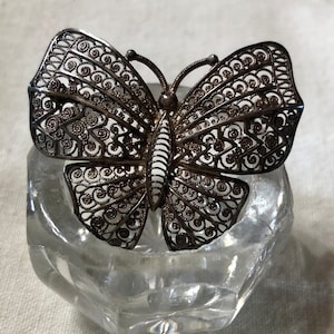 May include: A silver filigree butterfly brooch with intricate details. The brooch is made of delicate, interwoven silver wire, creating a delicate and intricate design.