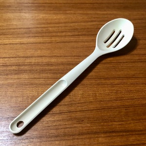 May include: A white plastic slotted spoon with a long handle. The spoon has three slots in the bowl.