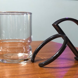 Op de afbeelding: Een zwarte plastic bekerhouder met twee ringen. De houder is ontworpen om om een ​​glas of mok te passen.