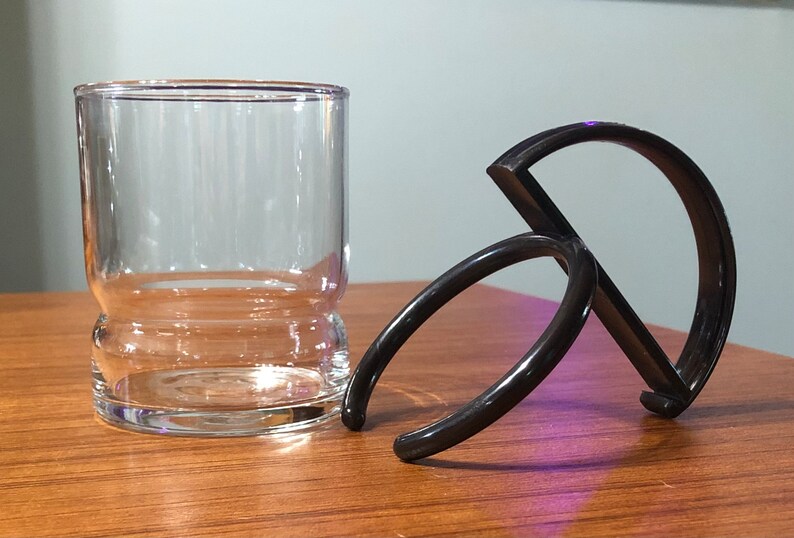 Op de afbeelding: Een zwarte plastic bekerhouder met twee ringen. De houder is ontworpen om om een ​​glas of mok te passen.