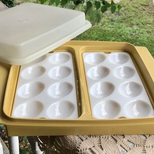 May include: A yellow plastic egg tray with a white lid. The tray has two rows of six egg-shaped compartments.