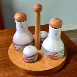 May include: A wooden stand with four ceramic containers. Two of the containers are tall and have a white background with a floral design. The other two containers are shorter and have a white background with a floral design. The stand has a wooden handle.