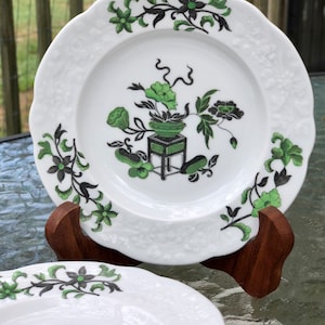 May include: Two white porcelain plates with a green and black floral design. The plates have a scalloped edge and are decorated with a floral motif.