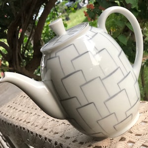 May include: White ceramic teapot with a geometric pattern of gray squares. The teapot has a lid and a spout.