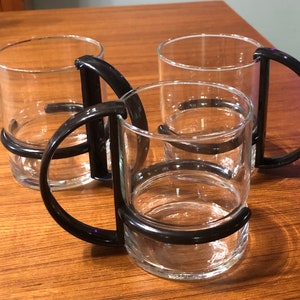 Op de afbeelding: Drie glazen bekers met zwarte kunststof handvatten. De bekers zijn op elkaar gestapeld.