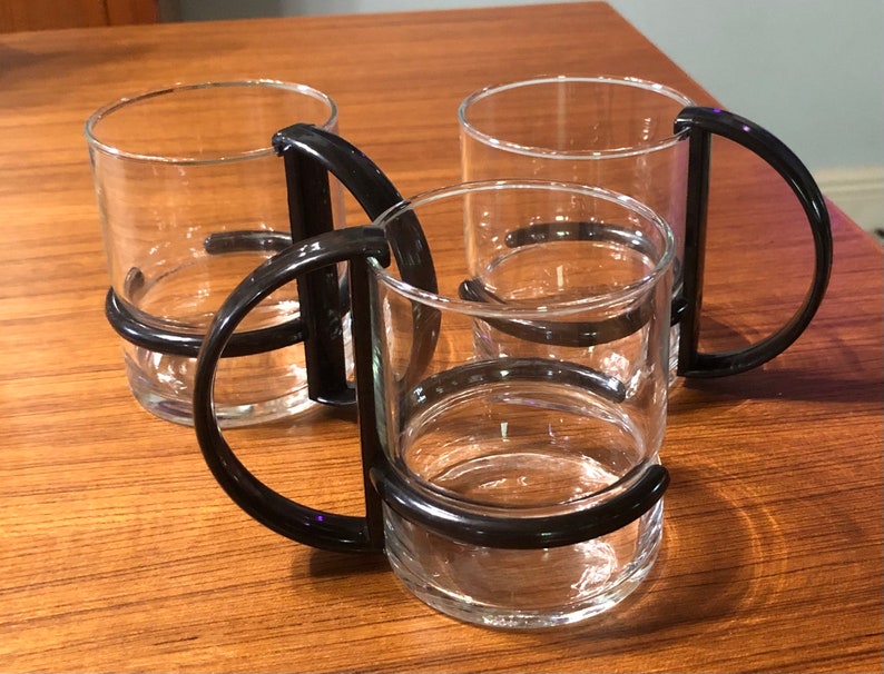 Op de afbeelding: Drie glazen bekers met zwarte kunststof handvatten. De bekers zijn op elkaar gestapeld.