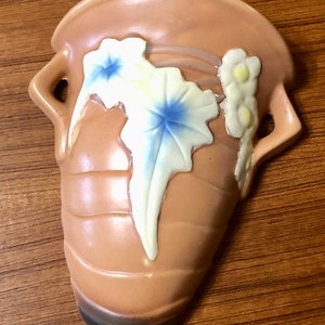 May include: A brown ceramic wall vase with a floral design. The vase has two handles and a brown glaze with white and blue flowers.