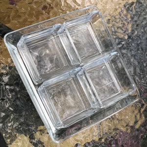 May include: A clear glass serving tray with four square compartments. The tray is made of thick glass and has a slightly raised edge.
