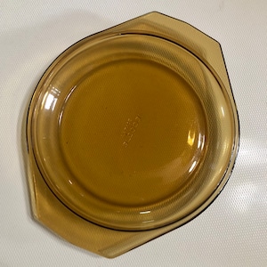 May include: A brown glass pie plate with a scalloped edge. The plate has the words "Pyrex" and "1 1/2 qt" printed on the bottom.