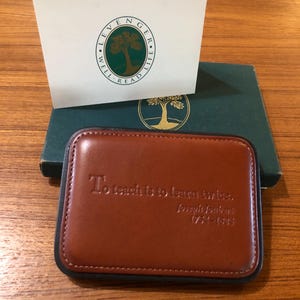 May include: A brown leather journal with a quote embossed on the front: "To teach is to learn twice." - Joseph Joubert 1754-1824. The journal is closed and has a black border.