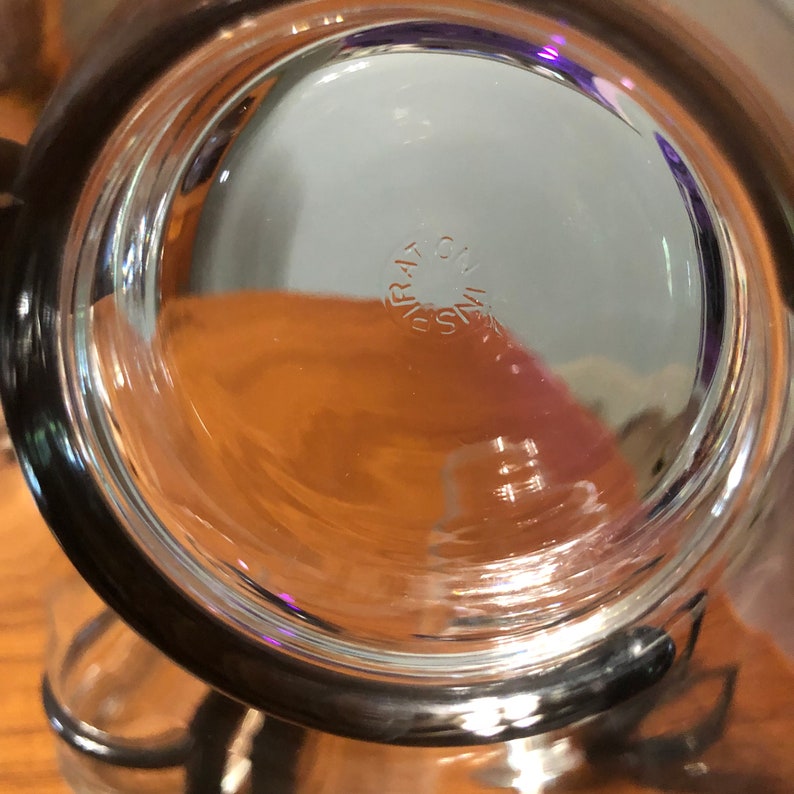 Op de afbeelding: Close-up van de bodem van een helder glazen drinkglas met een zwarte rand. Het glas heeft het woord "PYREX" op de bodem gedrukt.