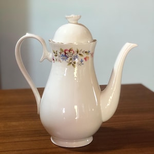 May include: White porcelain teapot with a floral design and a lid. The teapot has a gold trim around the lid and a delicate floral pattern on the body.