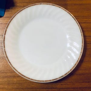 May include: A white ceramic plate with a gold rim and a rippled design. The plate is approximately 7 inches in diameter.