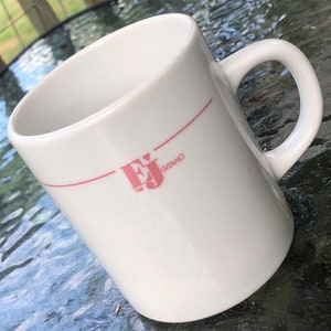 May include: White ceramic mug with a red line and pink logo that says "EJ Gitano TM" with a heart above the J.