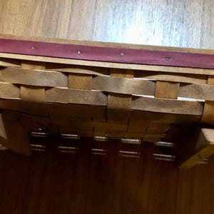 May include: A wooden basket with a red woven rim. The basket is folded in half and has two wooden legs.