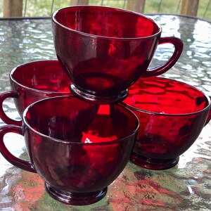 May include: Four red glass teacups stacked on top of each other. The cups are all the same size and shape, and they have a rounded bottom and a handle on the side.
