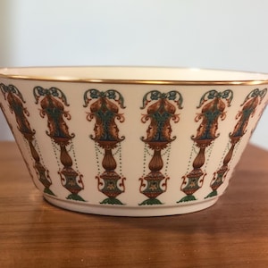 May include: A white ceramic bowl with a gold rim and a repeating pattern of green, brown, and blue stylized floral designs.