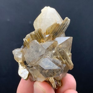 Puede incluir: Un grupo de cristales de cuarzo transparentes con inclusiones marrones. Los cristales están dispuestos en un racimo, con algunos de los cristales apuntando hacia arriba y otros hacia abajo. Los cristales son translúcidos y tienen un brillo vítreo.