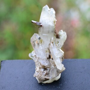 May include: A cluster of clear quartz crystals with a small piece of brown haematite. The crystals are arranged in a vertical formation, with the largest crystal at the top. The crystals are set on a dark background.