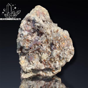 Puede incluir: Una muestra mineral en bruto, de forma irregular. La roca presenta una base de color beige claro y blanco, con secciones incrustadas de color marrón rojizo y estructuras cristalinas reflectantes. El logotipo "HEAVENMINERALSLTD" está en la esquina superior izquierda.
