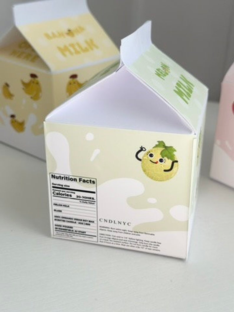 May include: A white cardboard milk carton with a green melon character on the front. The carton has a nutrition facts label on the side and the text "CNDLNYC" on the bottom.
