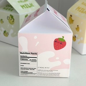 May include: A pink and white milk carton candle with a strawberry illustration and the text "Nutrition Facts" and "CANDLNYC".