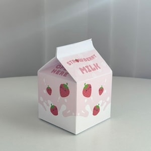 May include: A pink cardboard box shaped like a milk carton with the words "Strawberry Milk" printed on the front. The box is decorated with cartoon strawberries.