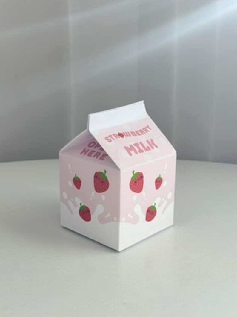 May include: A pink cardboard box shaped like a milk carton with the words "Strawberry Milk" printed on the front. The box is decorated with cartoon strawberries.