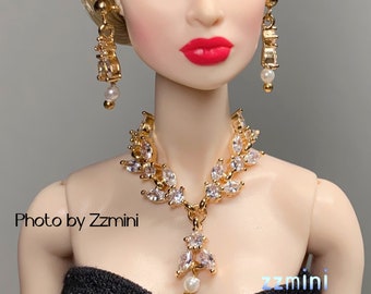 May include: A gold necklace with a pearlescent pendant and matching earrings. The necklace features a design of leaves with clear rhinestones. The earrings are drop earrings with a pearlescent bead at the bottom.