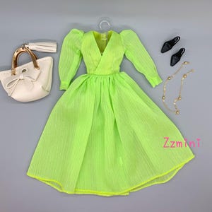 May include: A lime green dress with a V-neckline and long sleeves. The dress has a gathered skirt and is made of a sheer fabric. The dress is paired with a white handbag with a gold handle and a gold chain necklace with round beads. The outfit is completed with a pair of black heels.