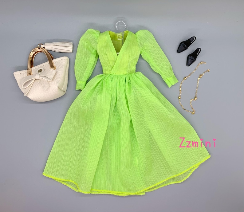 May include: A lime green dress with a V-neckline and long sleeves. The dress has a gathered skirt and is made of a sheer fabric. The dress is paired with a white handbag with a gold handle and a gold chain necklace with round beads. The outfit is completed with a pair of black heels.