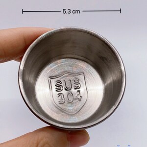 May include: A silver, round, stainless steel bowl with a diameter of 5.3 cm. The bowl has a shield-shaped logo on the bottom that says "SUS 304".