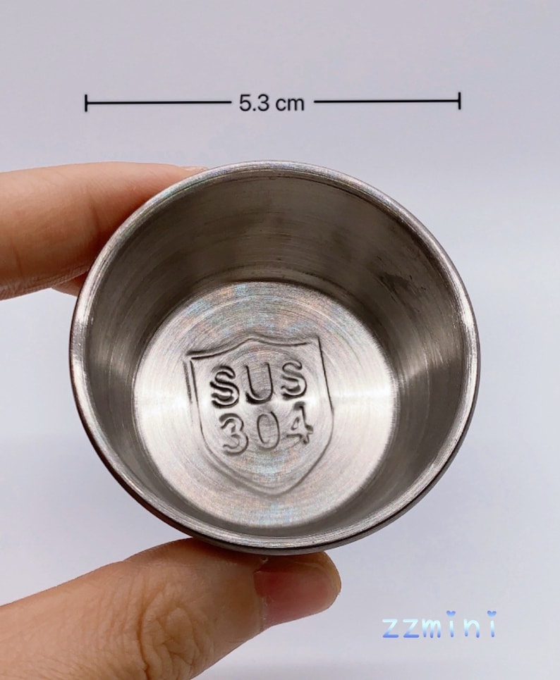 May include: A silver, round, stainless steel bowl with a diameter of 5.3 cm. The bowl has a shield-shaped logo on the bottom that says "SUS 304".