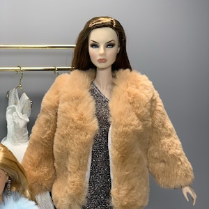 May include: A light brown faux fur jacket with a long sleeve and a collar. The jacket is open and shows a silver sparkly dress underneath.