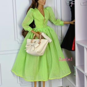 May include: A doll wearing a lime green dress with a white handbag and black heels. The doll is standing in front of a white closet with shelves.