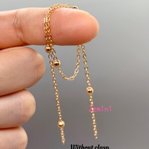 May include: Gold chain necklace with small round beads. The necklace is layered and has a delicate design. It is without a clasp, allowing for versatile styling.