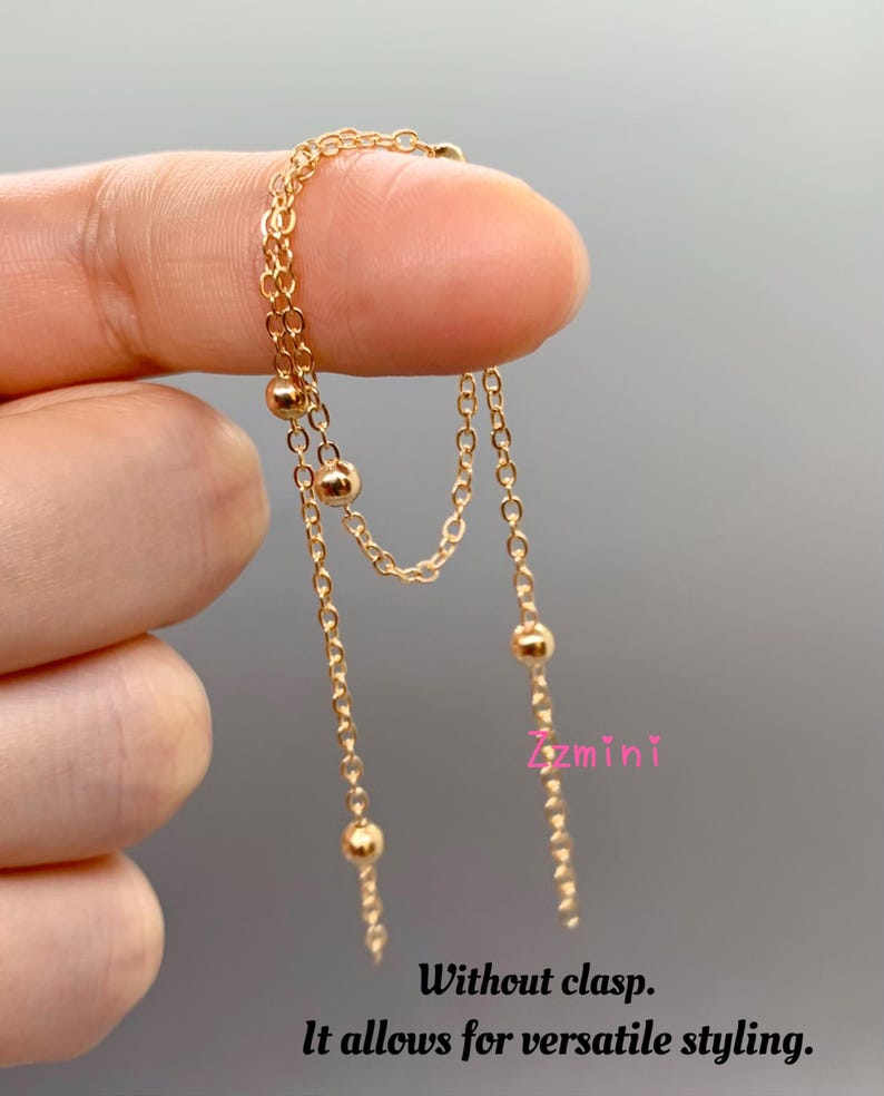 May include: Gold chain necklace with small round beads. The necklace is layered and has a delicate design. It is without a clasp, allowing for versatile styling.